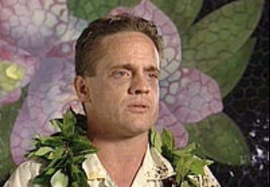 Portrait of ceramic tile artist Robert Vogland wearing a maile lei in front of one of his hibiscus tile murals